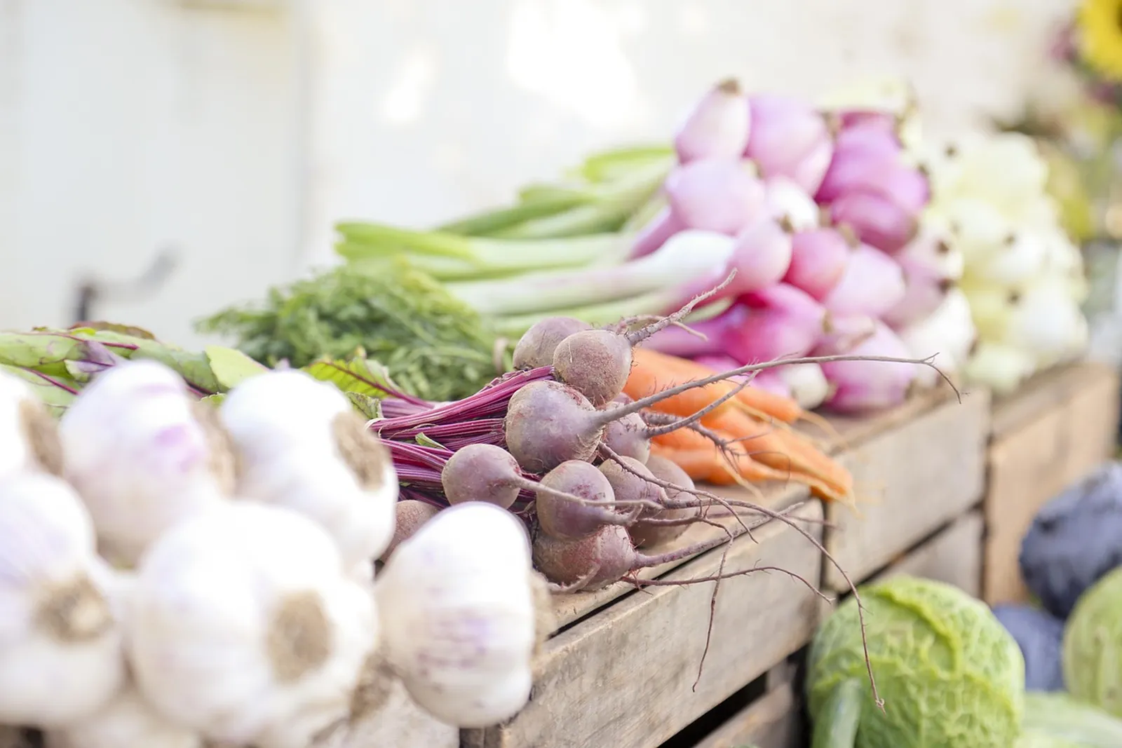 Garlic, beets, onions and carrots in a wooden crate at a produce stand
